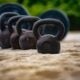 Cast iron kettlebells lined up by weight on a concrete surface with a barbell in the background — equipment for a beginner kettlebell workout
