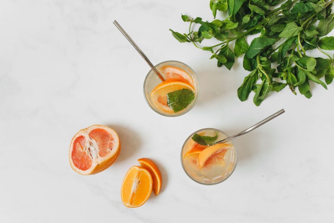 A refreshing drink in a clear glass, surrounded by colourful fruits and herbs.
