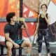 Man sitting on a gym bench drinking from a bottle between sets with a kettlebell at his feet, woman drinking behind him