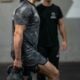 Man holding a kettlebell in a gym while a trainer watches