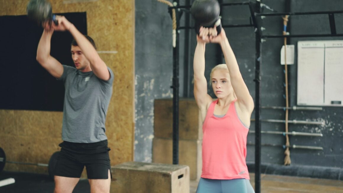 Man and woman performing kettlebell swings in a gym