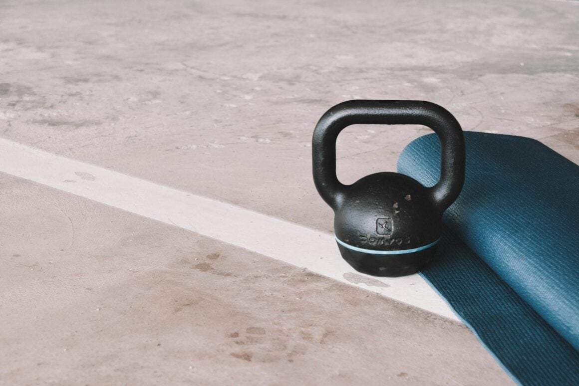 Black kettlebell resting on a concrete floor beside a rolled exercise mat
