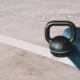 Black kettlebell resting on a concrete floor beside a rolled exercise mat