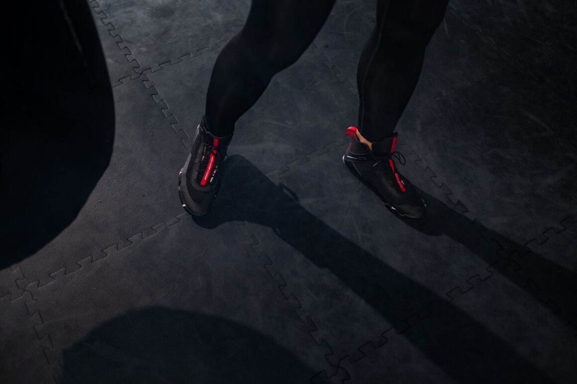 Thin, flat boxing boots on a dark gym floor, the kind of low, firm shoe that works for squats, deadlifts and kettlebell training