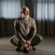 Grey-bearded man in his fifties squatting with a kettlebell between his feet in a dark studio