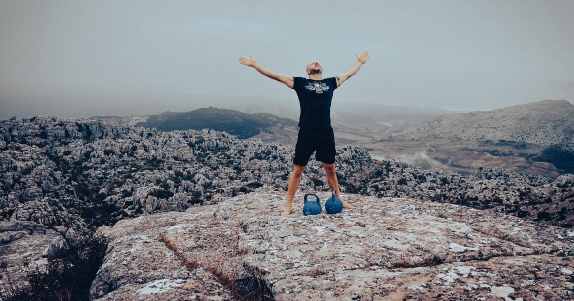 Taco Fleur standing with arms spread wide on the summit of El Torcal, two kettlebells at his feet