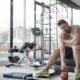 Tired man sitting on a gym bench between sets, head resting on his hand, holding a red kettlebell on the floor