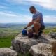 Man sitting beside two kettlebells on a rocky mountain overlook