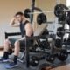 Tired man in a black tank top resting on a weight bench between sets in a home gym